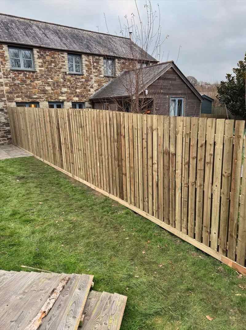 A long run of new featheredge fencing along a lawn, with cottages behind