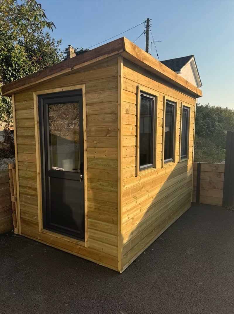 A tall timber garden room with a glazed door and three windows