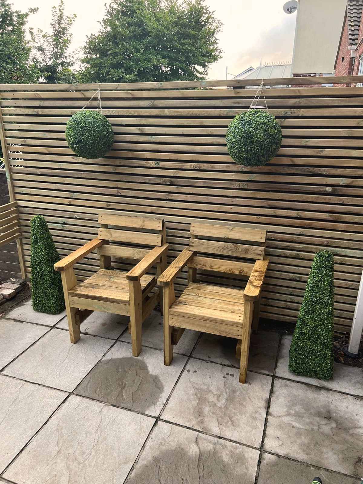 Two new tanalised timber garden chairs against a slatted fence