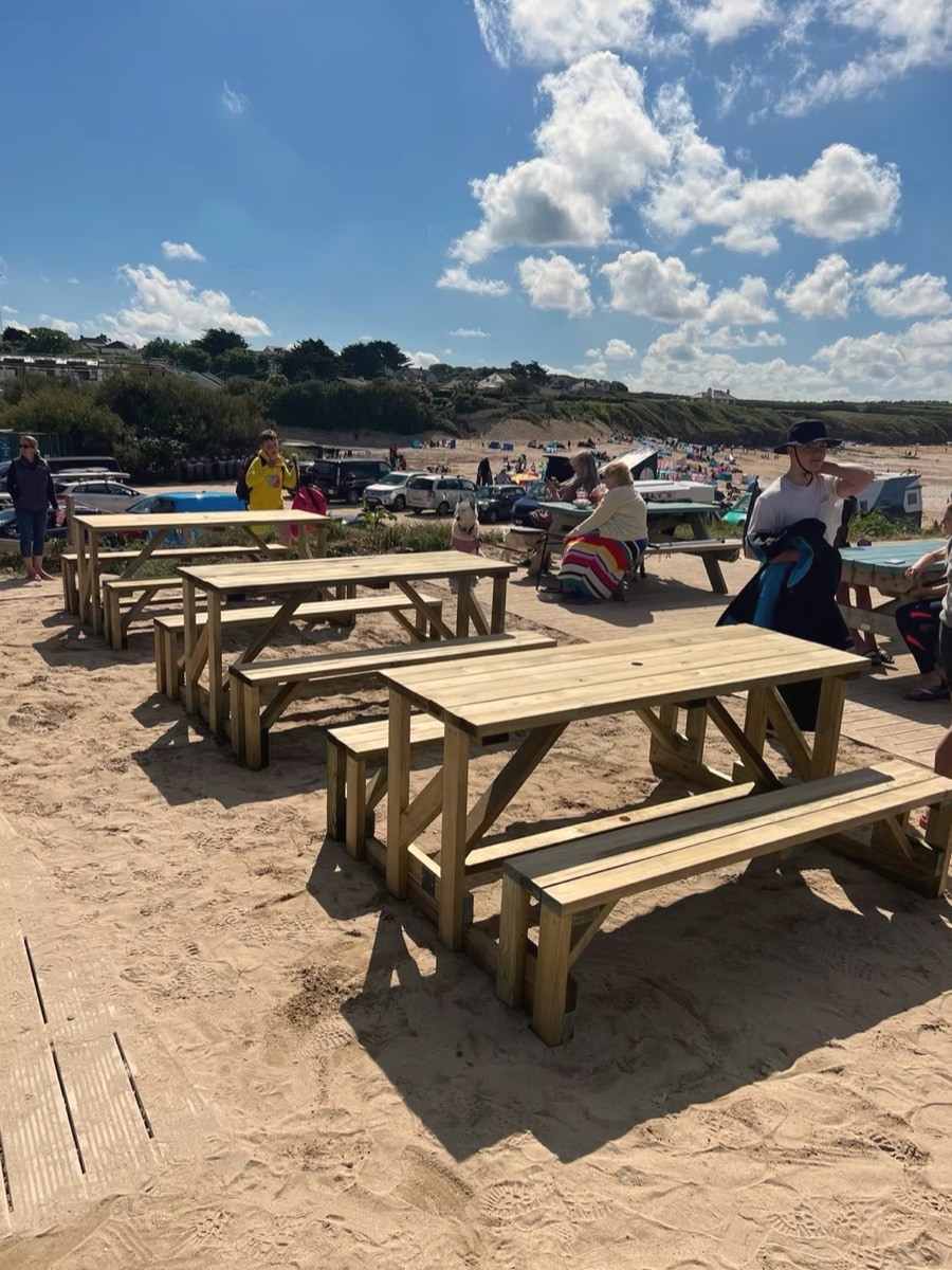 A row of timber picnic benches set out on sand by the sea