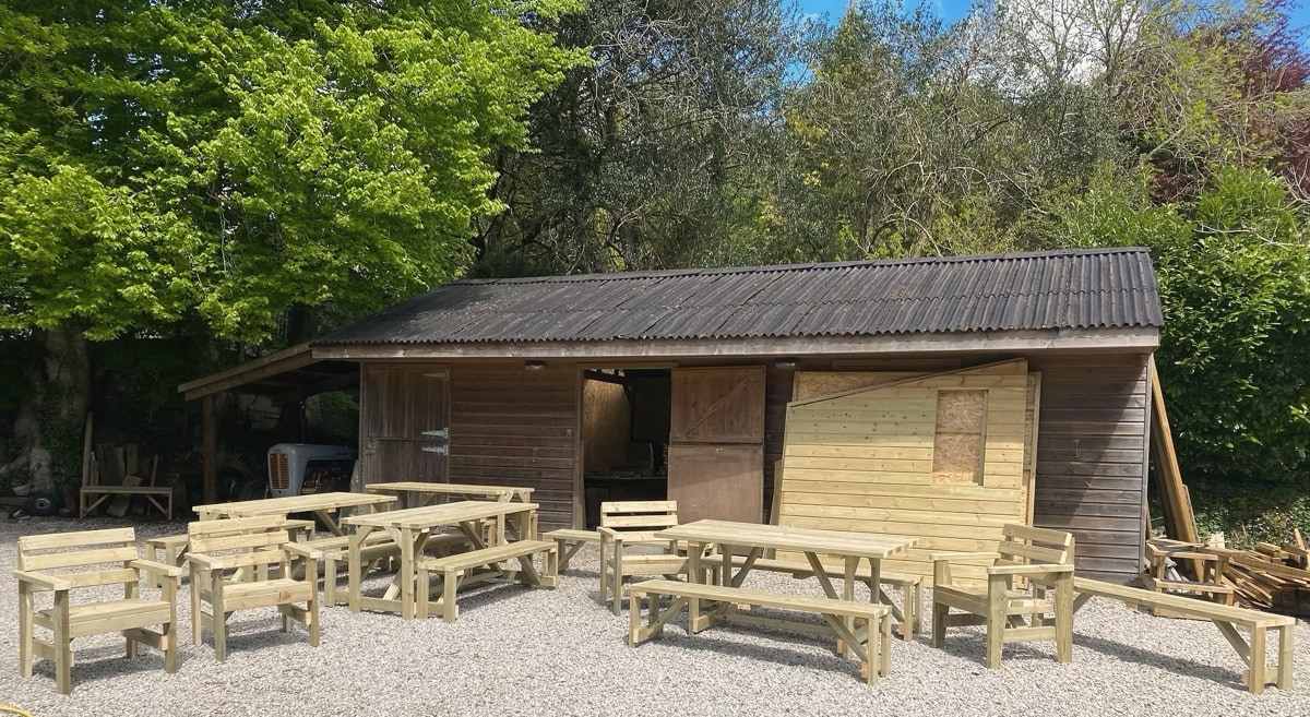 Handmade benches and tables lined up on gravel in front of the Turps Wood Design workshop in Lostwithiel