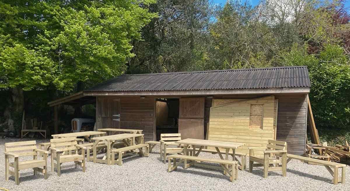 Handmade benches and tables lined up on gravel in front of the workshop in Lostwithiel