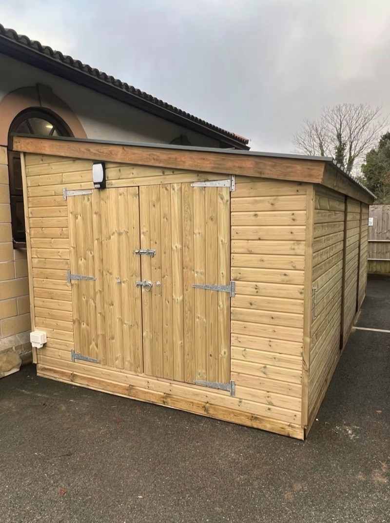 A long pent-roof shed with double doors and an outside light, on a drive