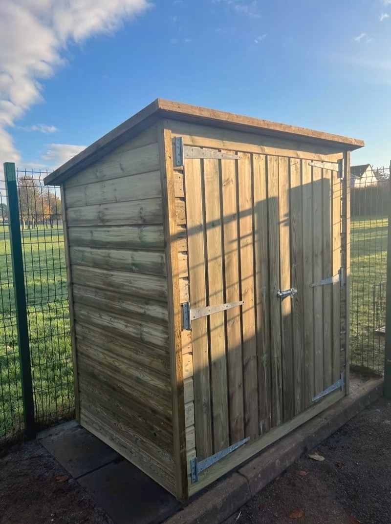 A tall pent-roof shed with double doors beside a fence