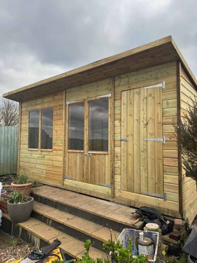 A pent-roof workshop with three windows and a door, steps up to it